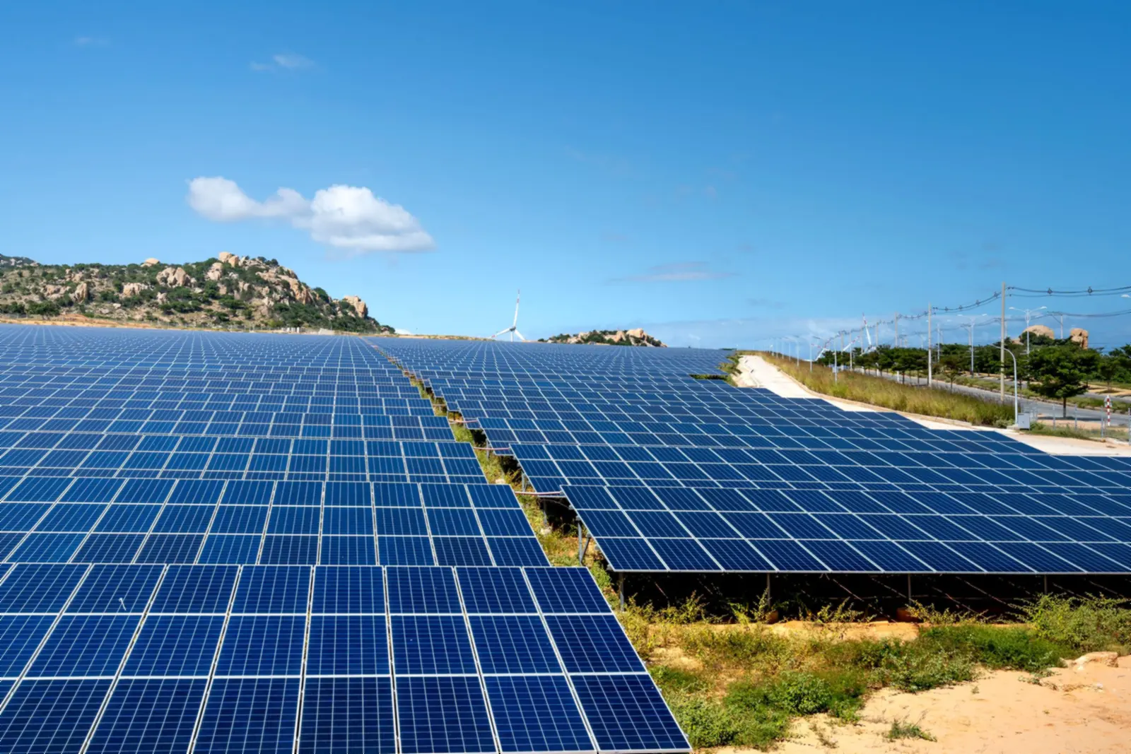Centrale photovoltaïque au sol sous un ciel bleu, avec des collines rocheuses en arrière-plan
